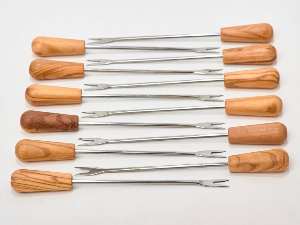 Douze piques à deux dents en acier inoxydable avec manches en bois d’olivier, disposés à plat.